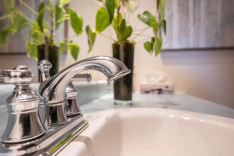 Close-up of a bathroom faucet slowly dripping water, symbolizing plumbing issues that need a professional plumber in Canada.