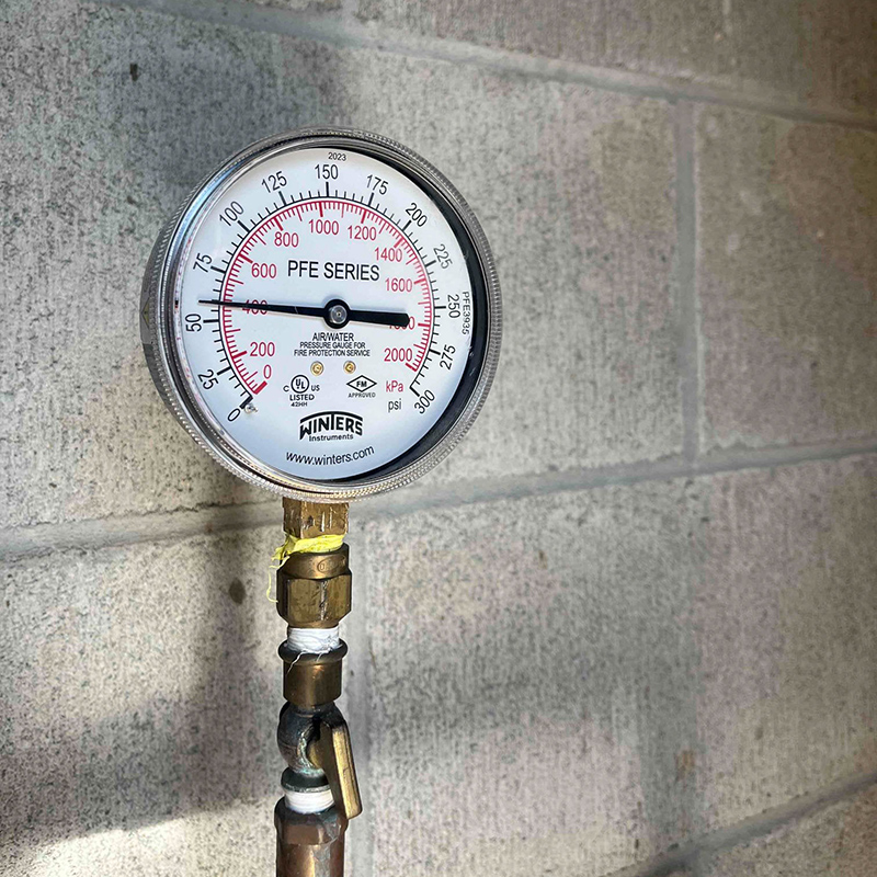 A Winters brand pressure gauge shown against grey concrete bricks