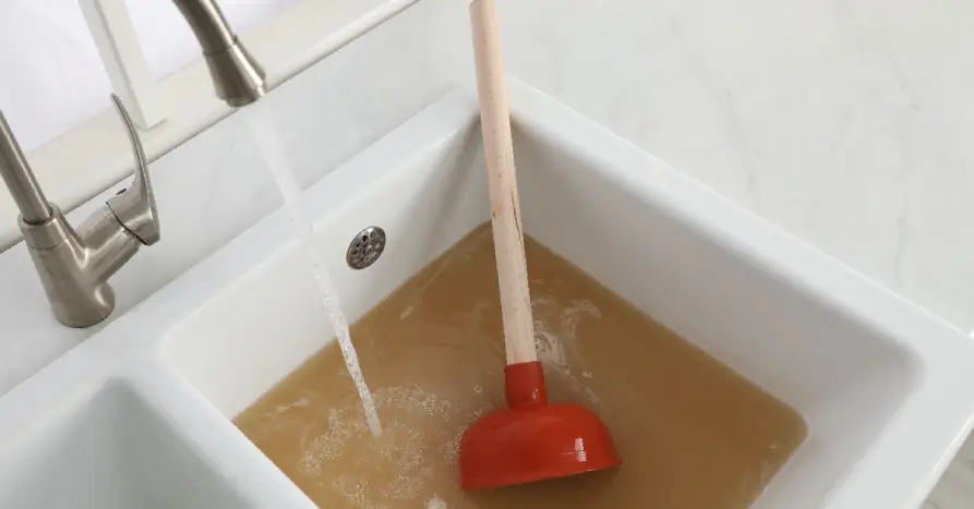 A plunger sitting in a sink filled with dirty water from a sewer backup in Scarborough, ON
