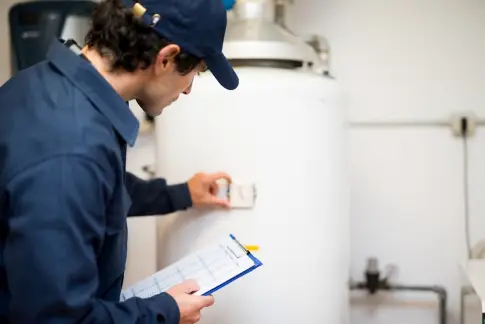 A plumber inspecting a home’s hot water tank and marking details off on a clipboard during a plumbing inspection.